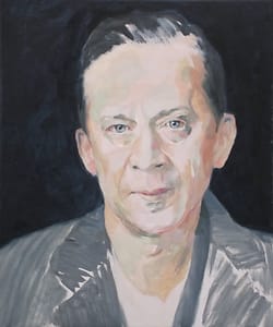 Middle age man wearing a gray jacket looking indignified, with a black background.